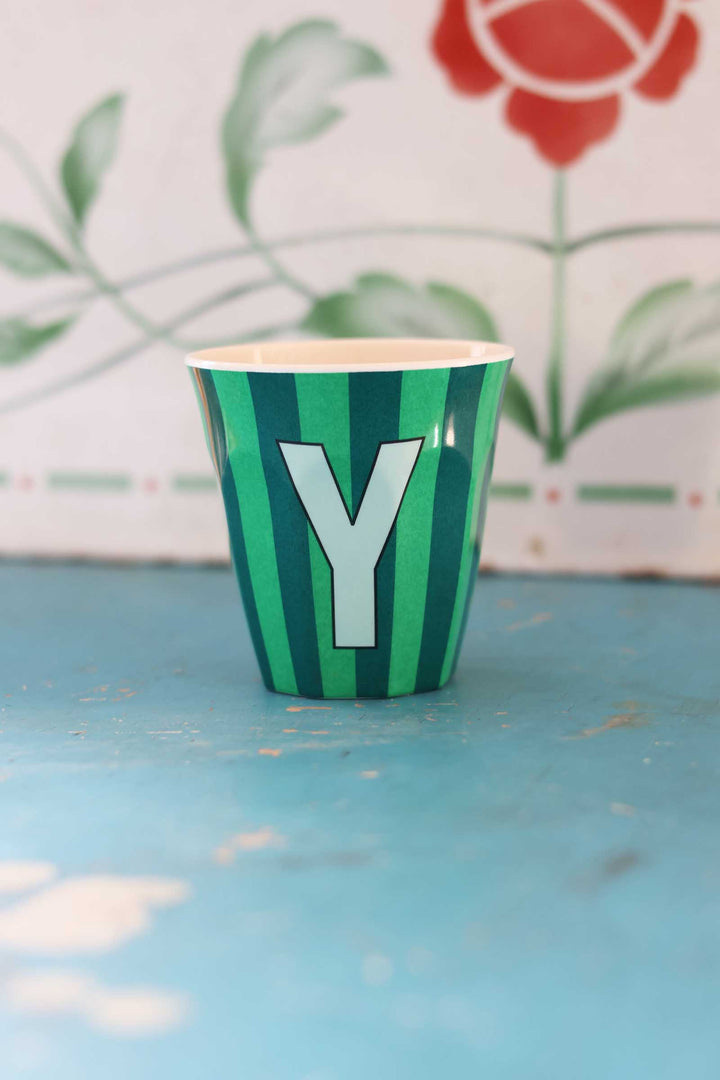Green striped cup with letter 'Y' on a blue surface with floral background