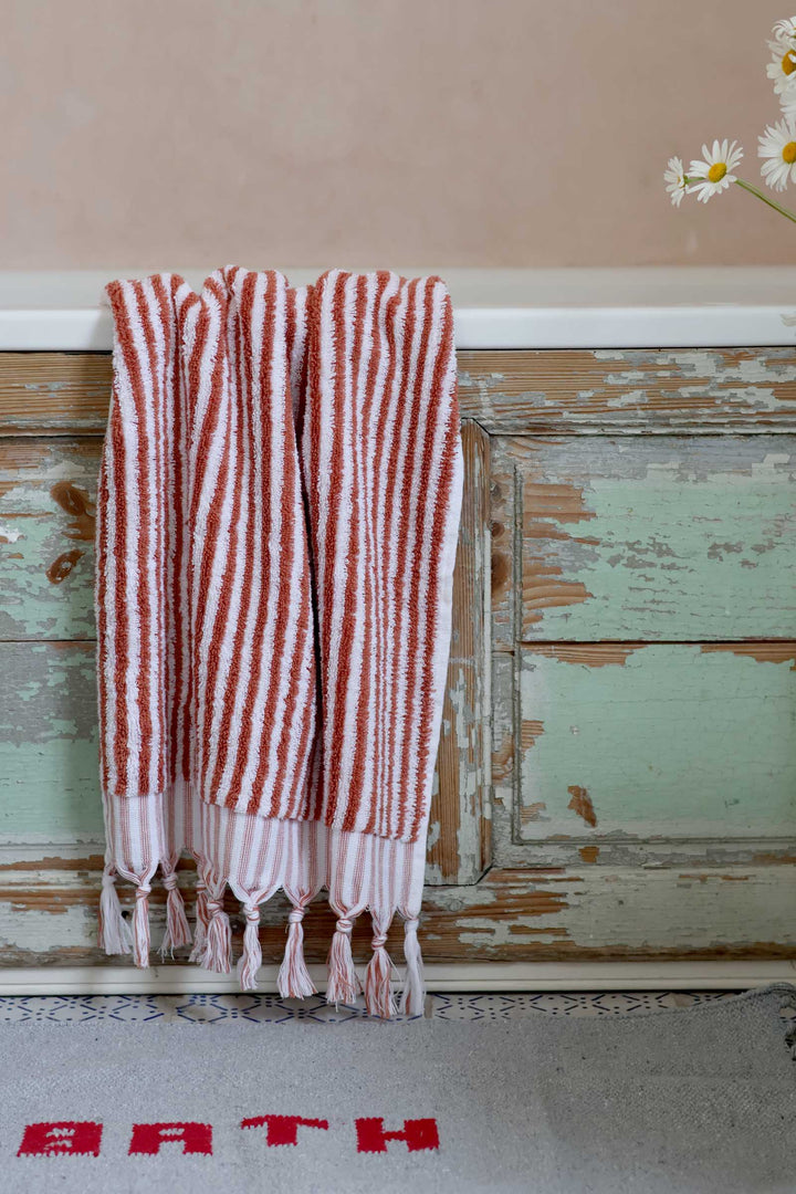 Striped towel with tassels hanging on a wooden surface with 'Bath' text below.