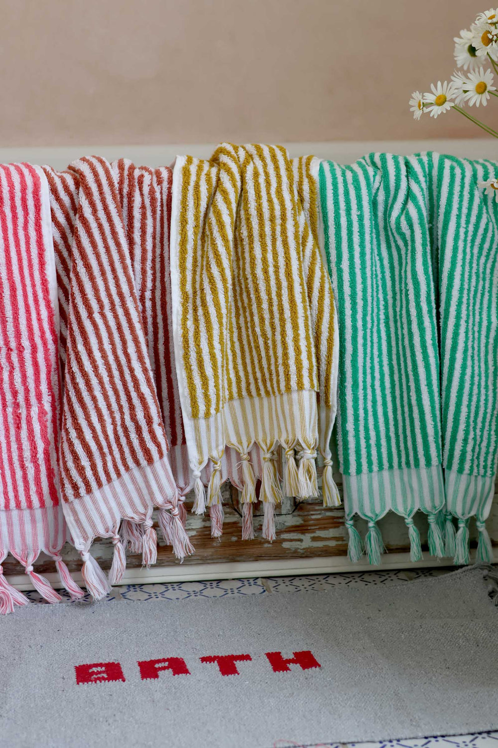Three striped towels in red, yellow, and green hanging on a rack with a bath mat below.