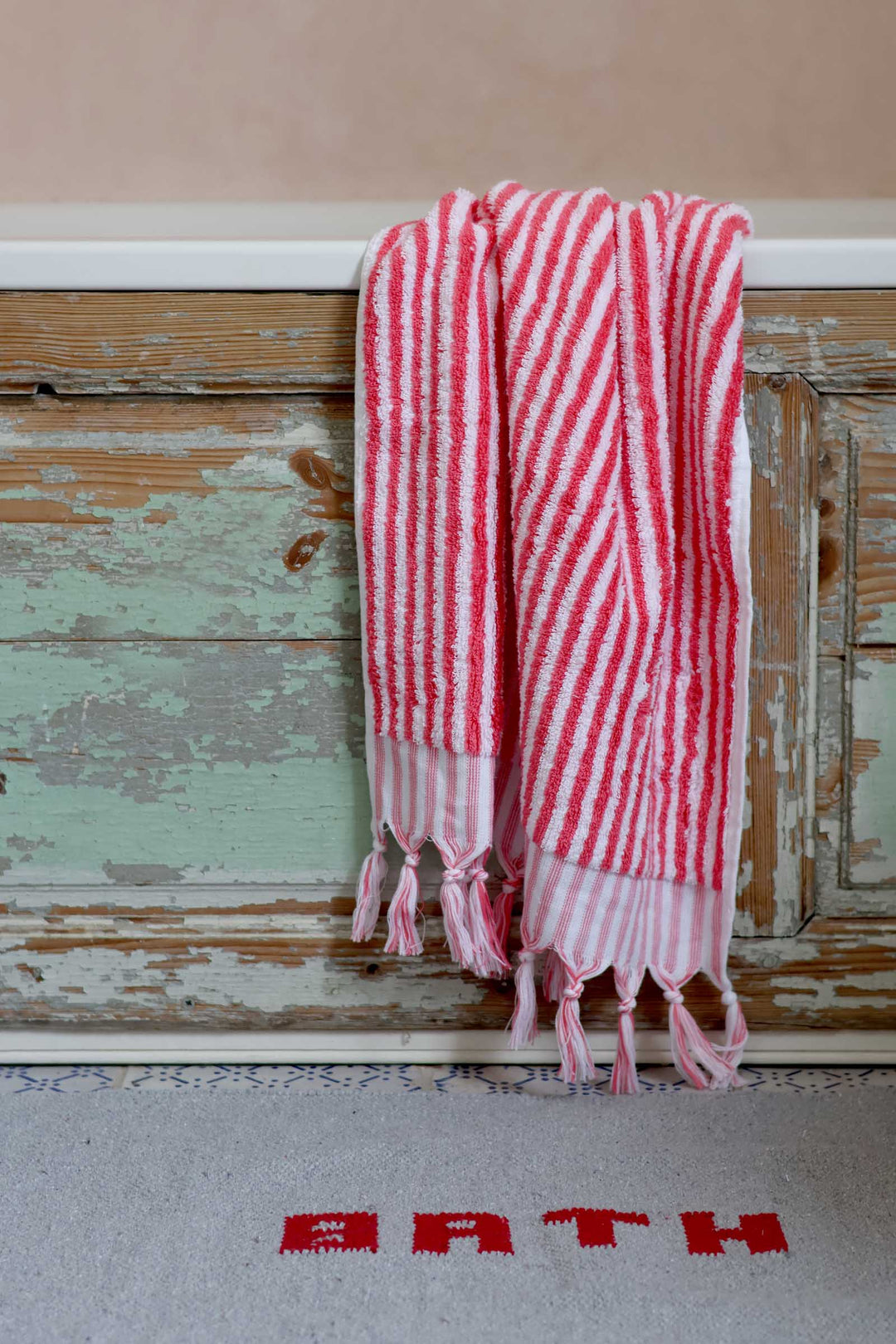 Red and white striped towel hanging on a wooden door with 'BATH' rug below.