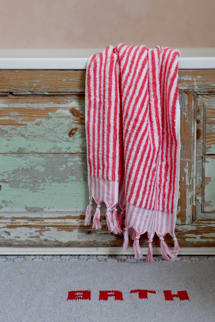 Red and white striped towel hanging on a wooden door with 'BATH' rug below.