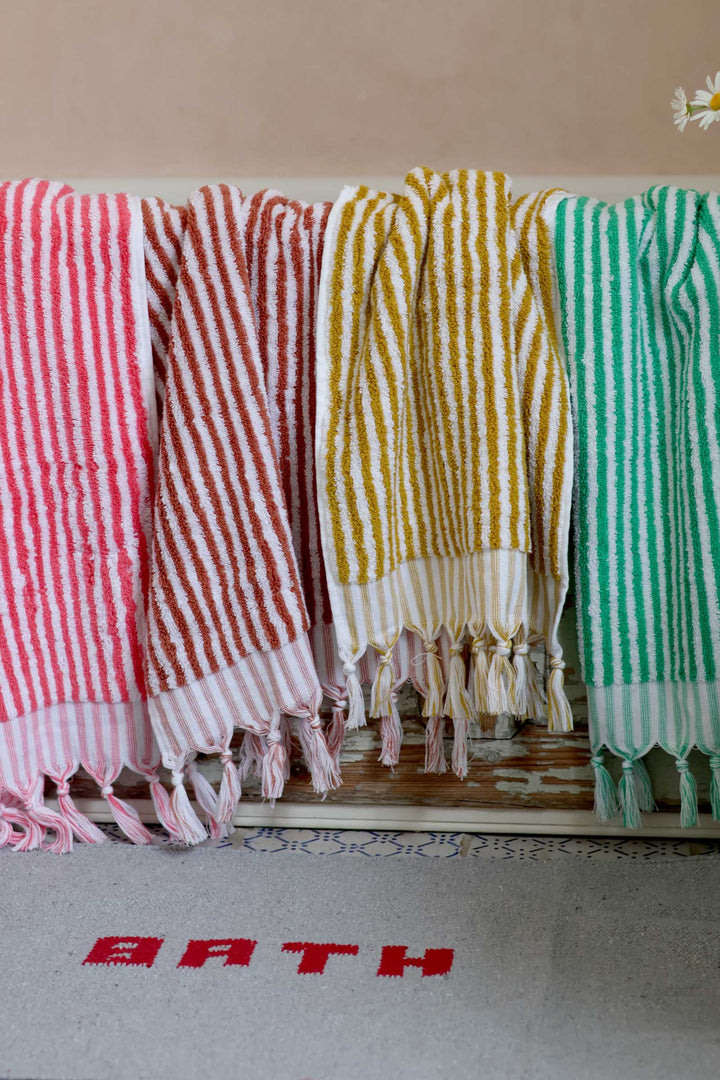 Colorful striped towels hanging on a rack with a 'BATH' mat below.