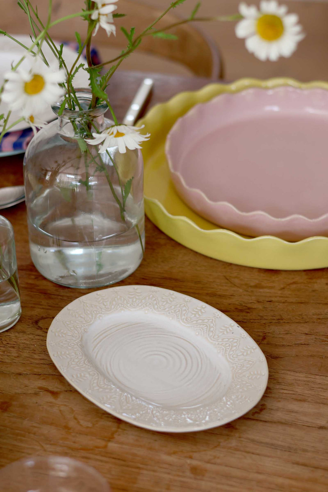 Table setting with plates, a vase of flowers, and a pink plate in the background.