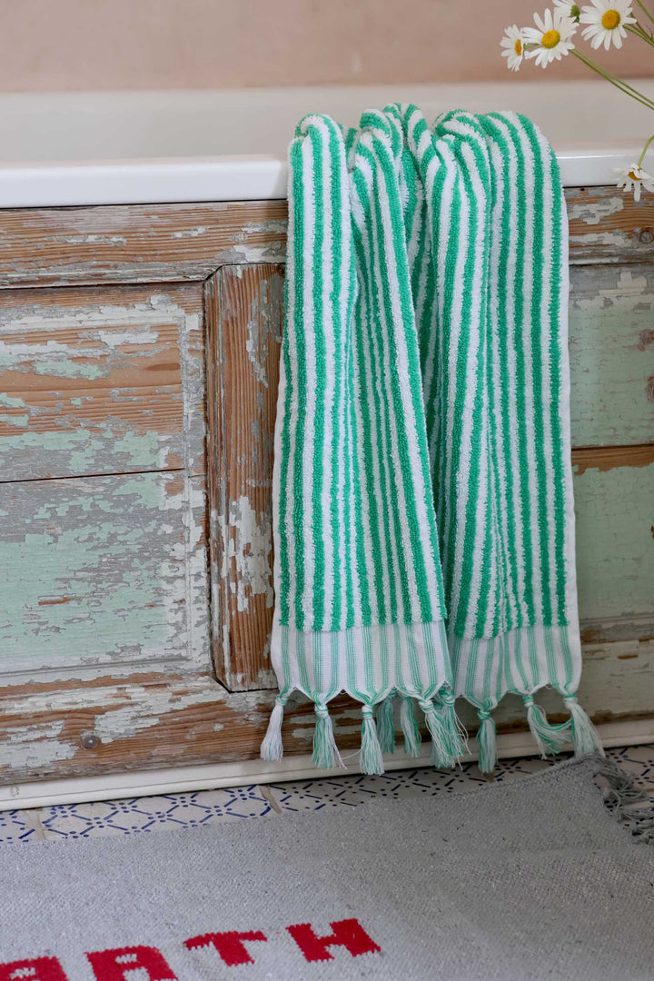 Green and white striped towel with tassels hanging on a wooden surface.