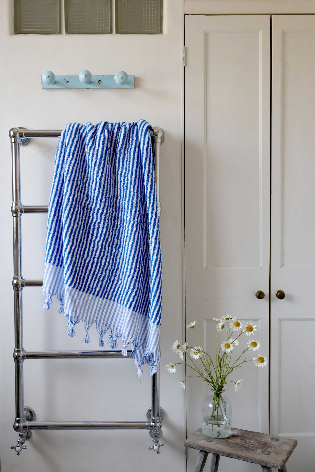 Towel rack with a blue and white striped towel, white door, and small table with flowers in a room.