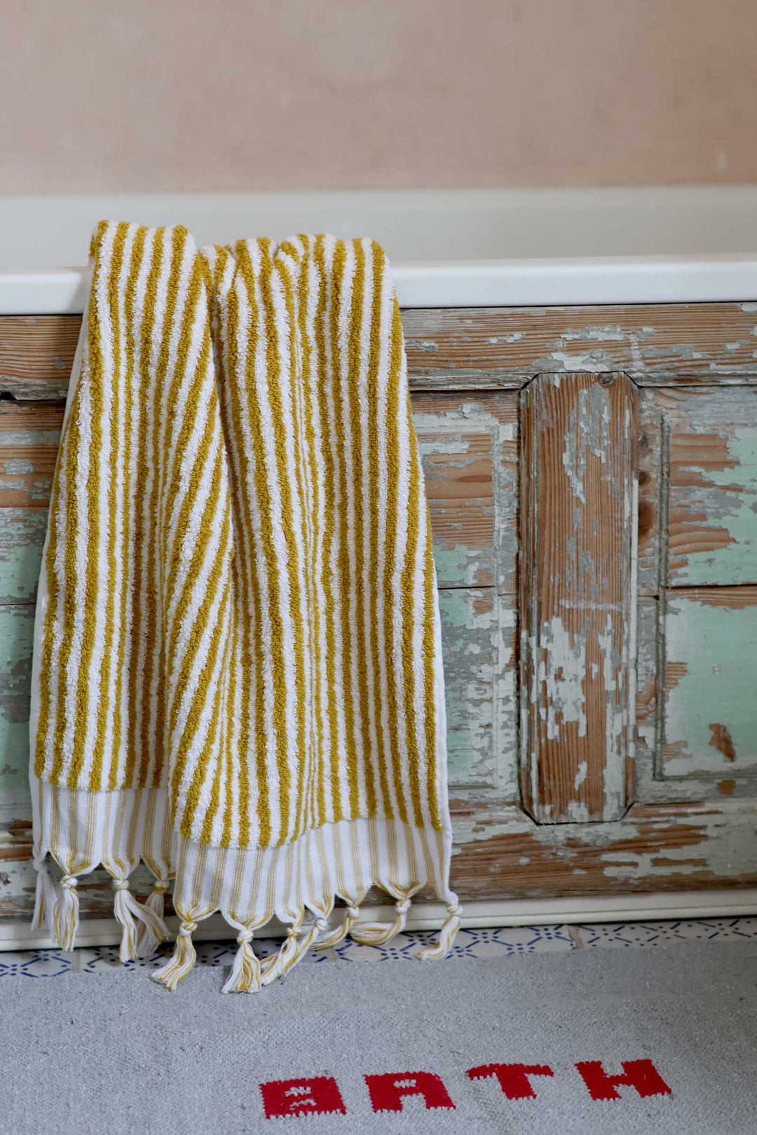 Striped towel hanging on a wooden door with 'BATH' rug below