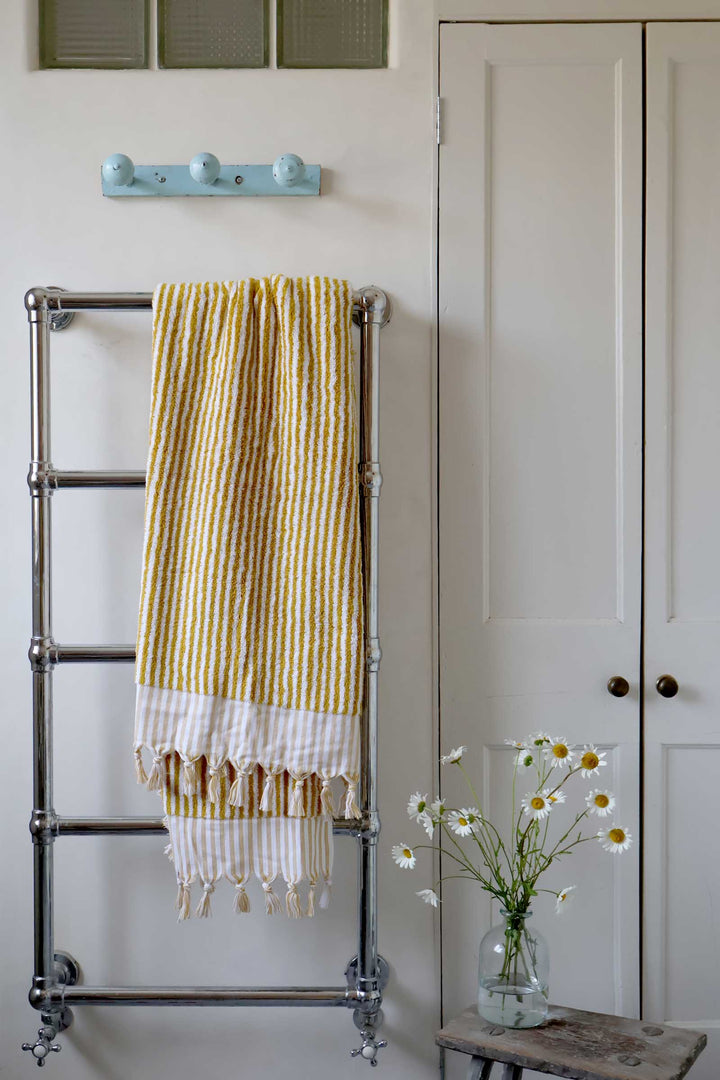 Yellow and white striped towel on a metal towel rack with a vase of daisies on a wooden stool.
