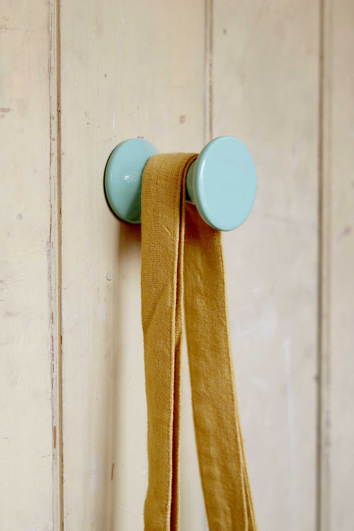 Two turquoise wall hooks with a mustard yellow scarf on a wooden background