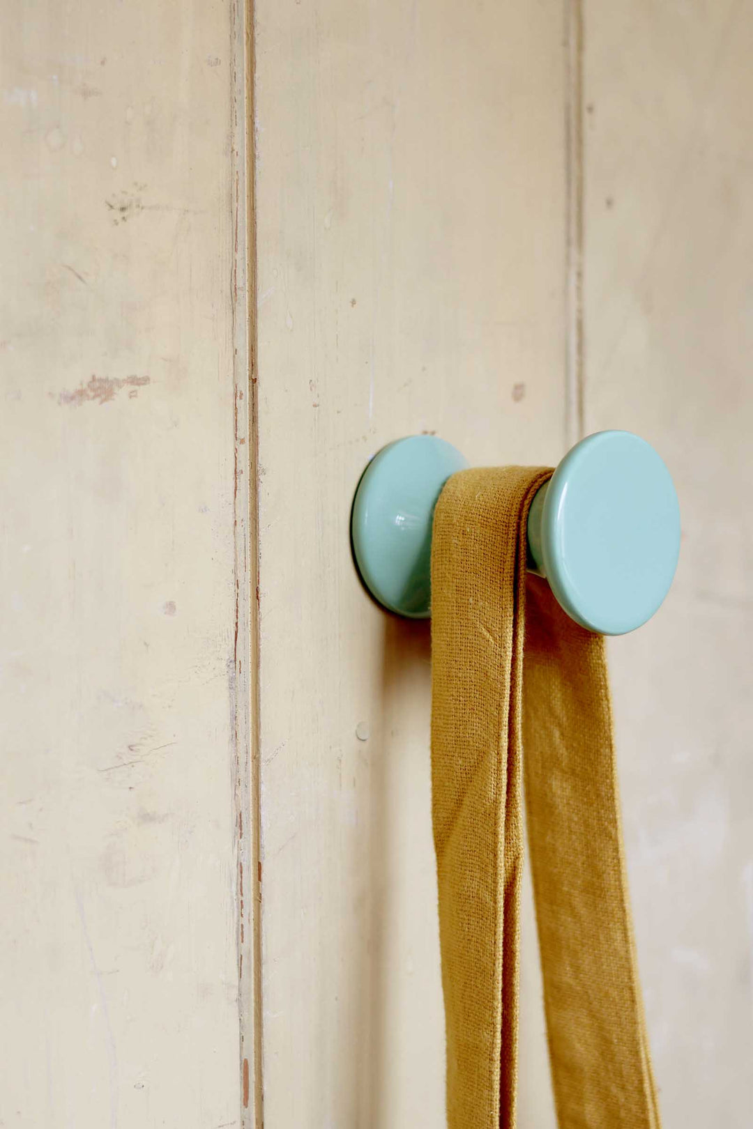 Light blue wall hook with a mustard yellow scarf on a wooden background