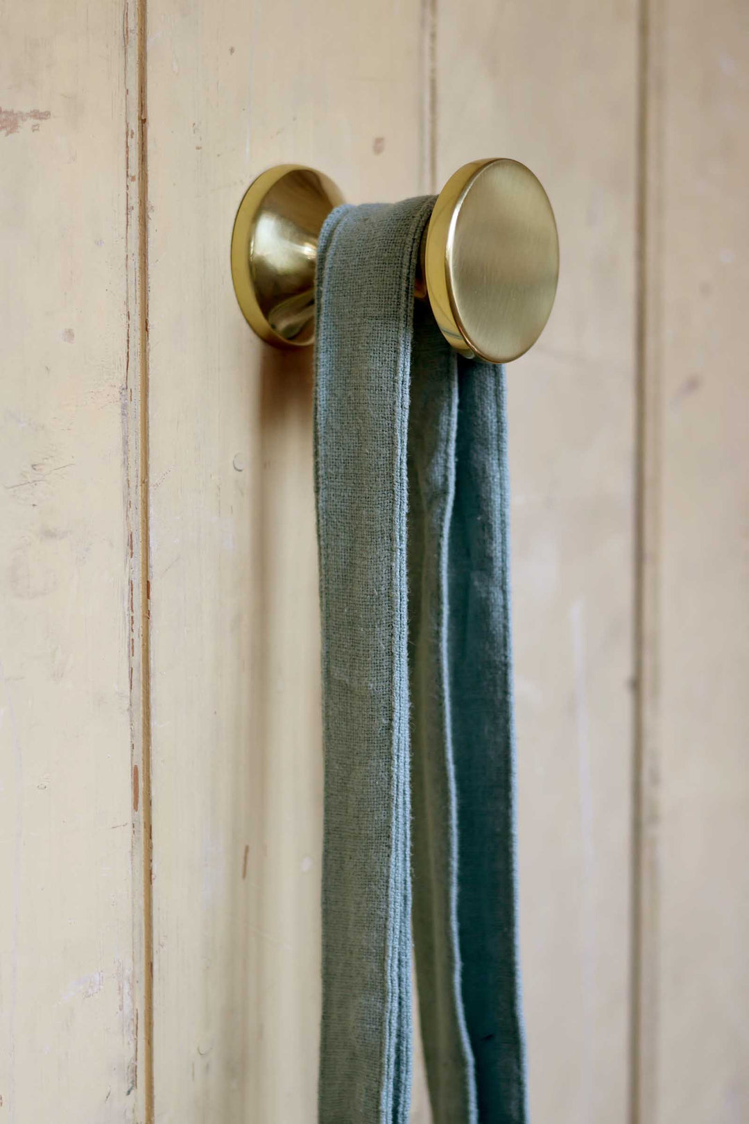 Brass wall hook with a green ribbon on a wooden background