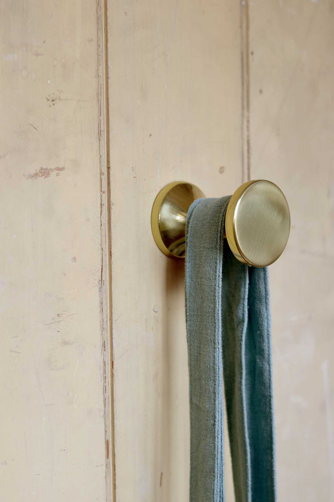 Brass hook on a wooden door with a green towel hanging from it