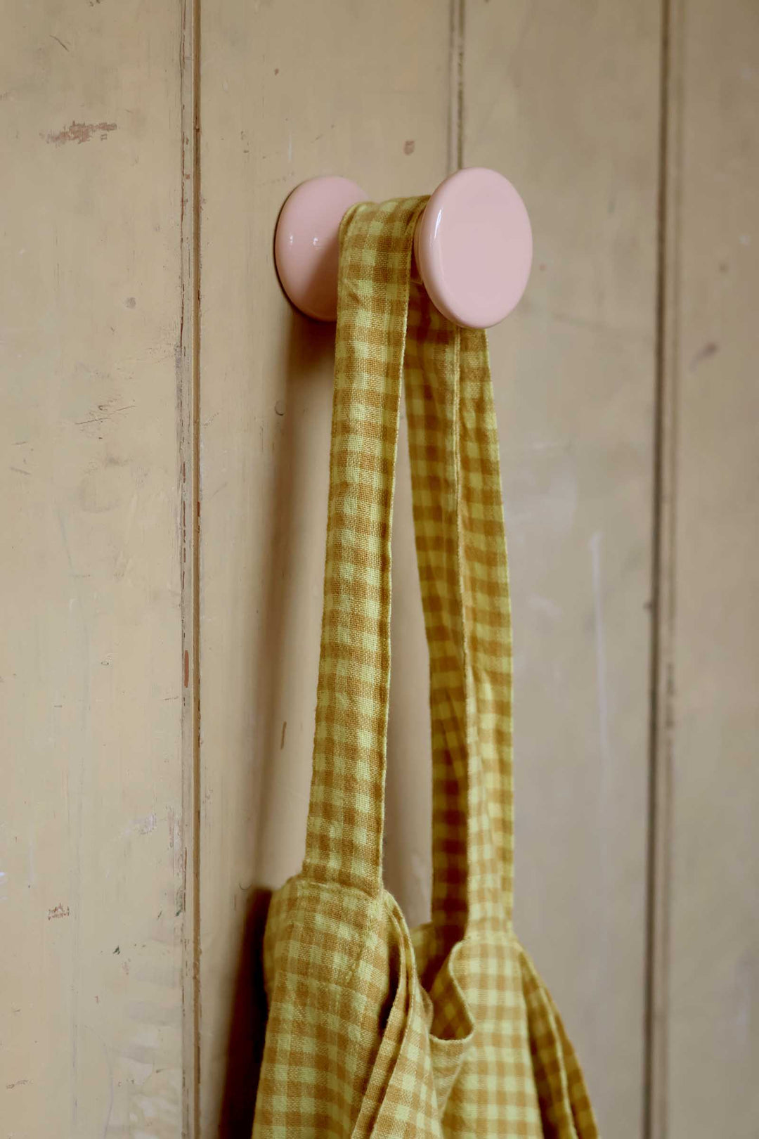 Pink wall hook with a yellow checkered towel on a wooden background