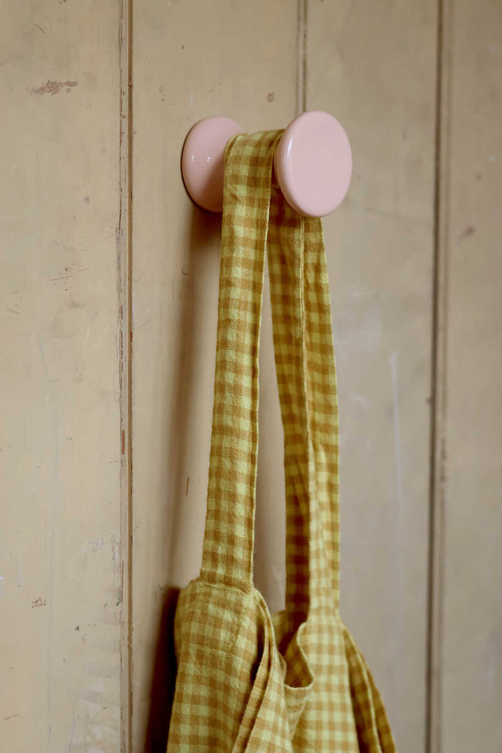 Pink wall hook with a yellow checkered towel on a wooden background