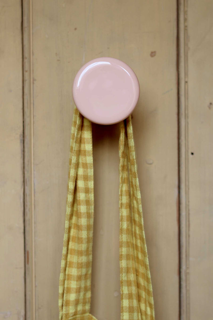 Pink round hook on a wooden door with a green and yellow checkered cloth hanging from it.