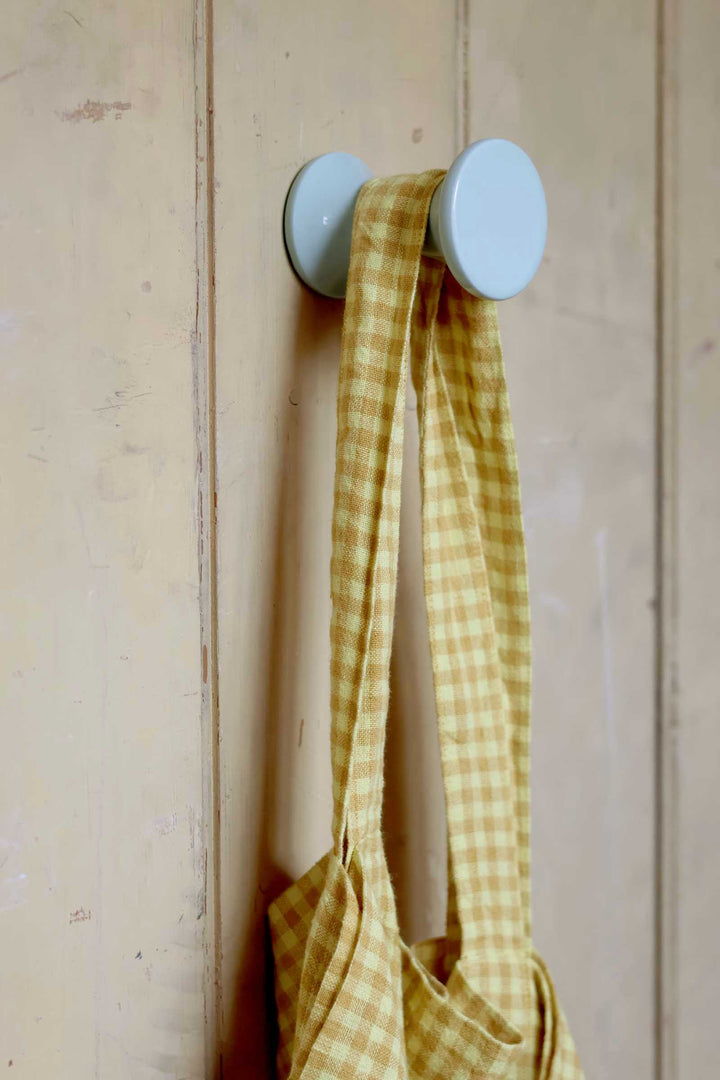 Yellow checkered bag hanging on a white hook against a wooden wall.