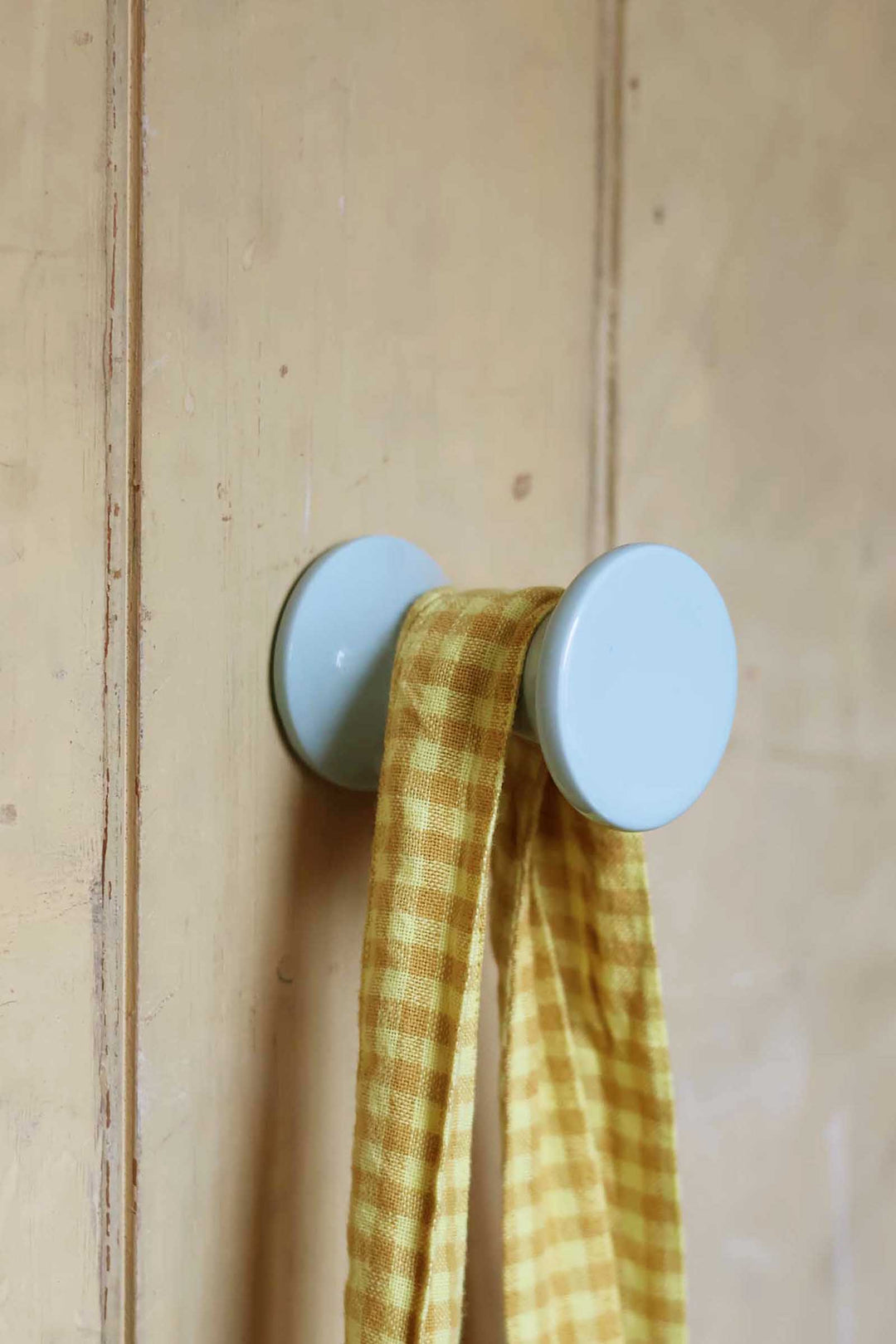 Two light blue wall hooks with a yellow checkered cloth on a wooden background