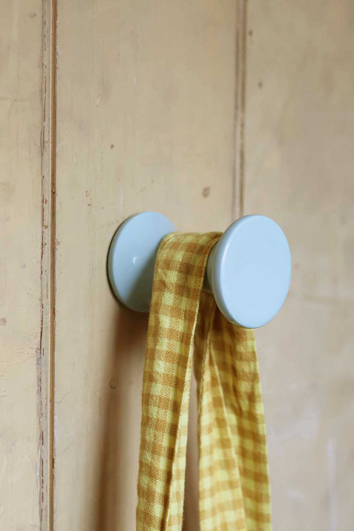 Two light blue wall hooks with a yellow checkered cloth on a wooden background