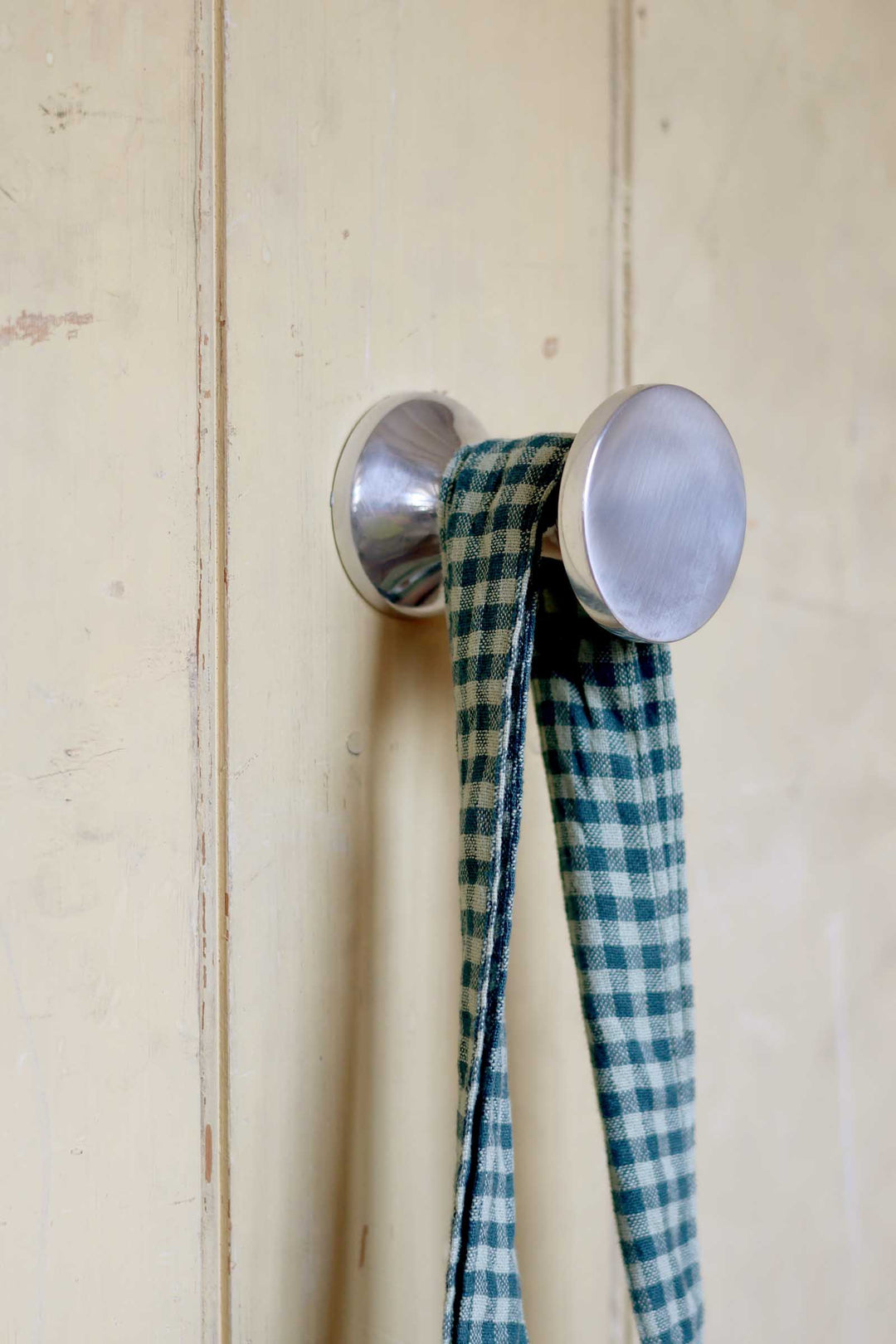 Metallic hook with a blue and white checkered ribbon on a wooden surface