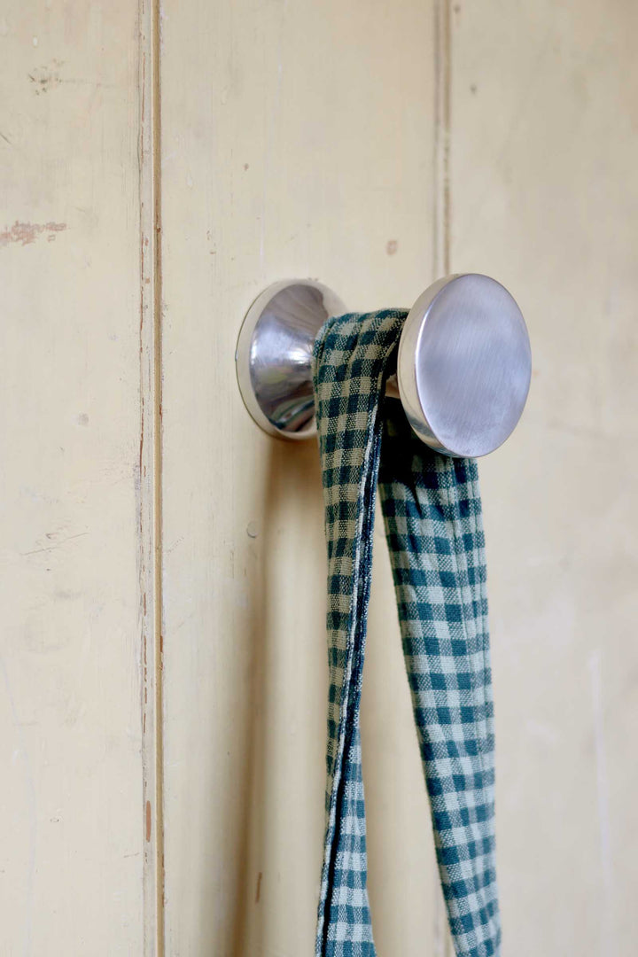 Metallic hook with a blue and white checkered ribbon on a wooden surface