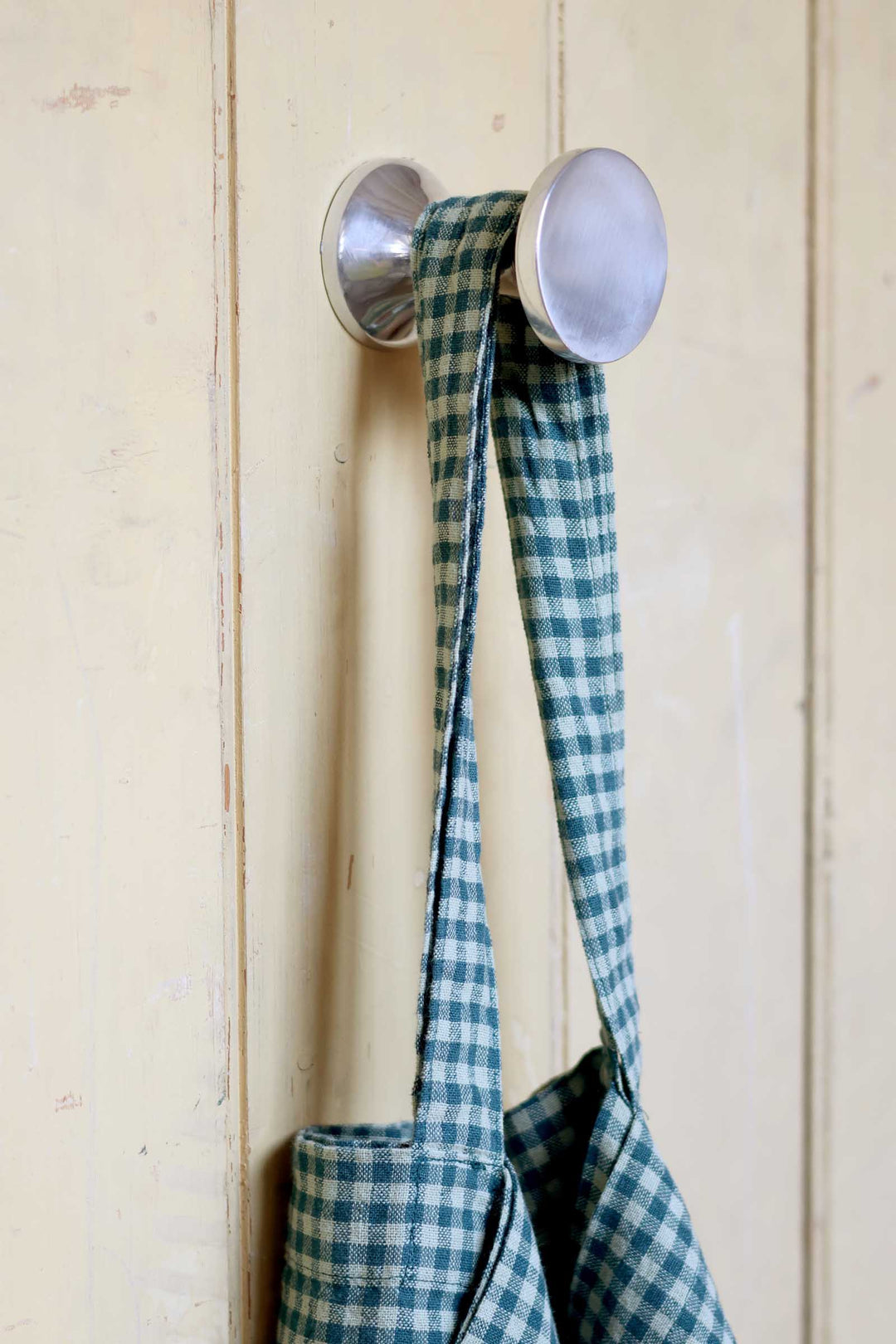 Metallic hook with a blue and green checkered apron on a wooden background