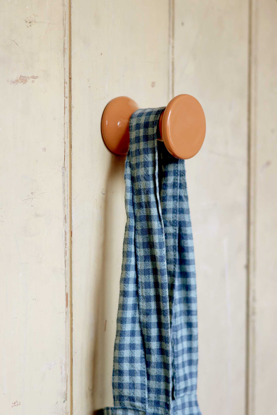 Blue plaid towel hanging on a wooden hook against a light wooden panel background