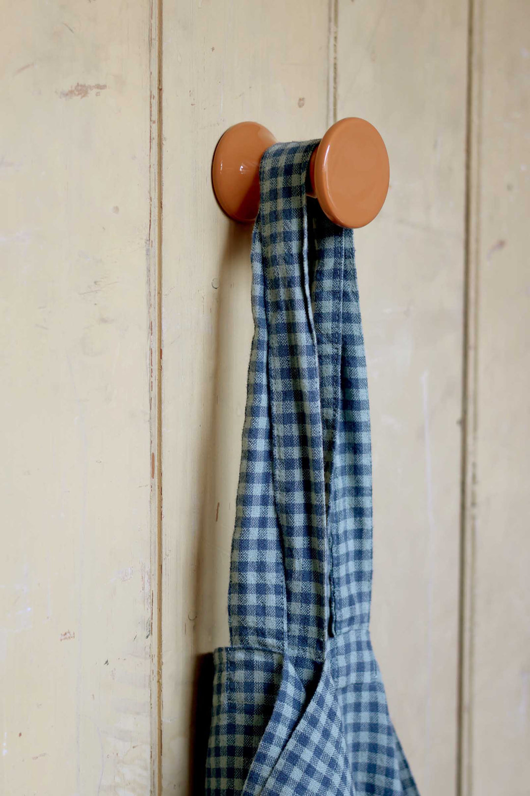 Blue checkered towel hanging on a wooden hook against a white wooden panel background
