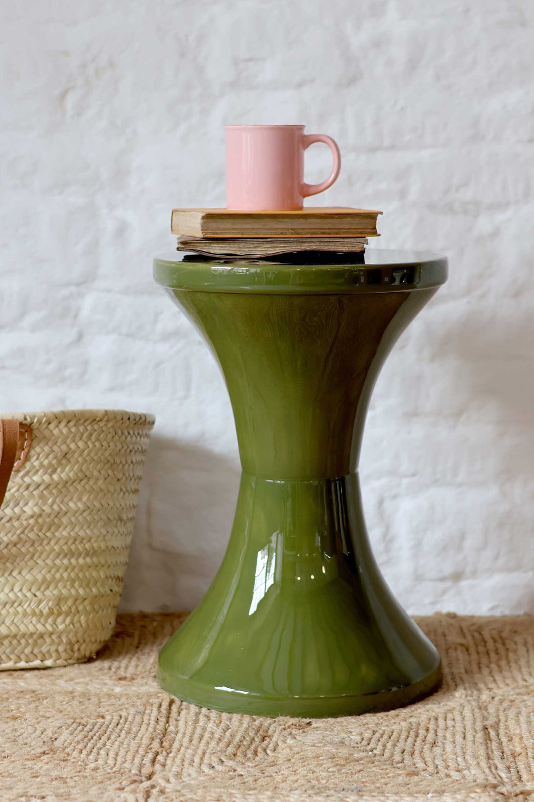 Green side table with a pink cup and books on a textured surface