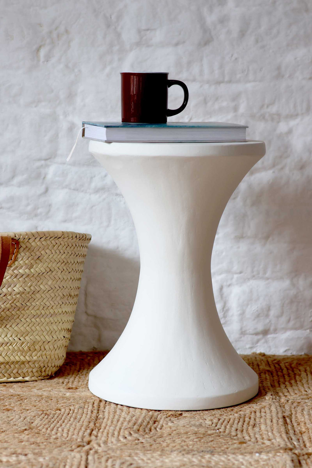 White side table with a red mug and book on a textured surface