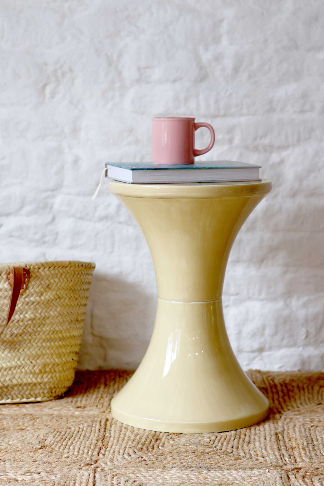 Yellow side table with a pink mug on a textured white wall background