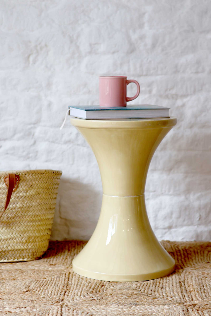 Yellow side table with a pink mug on a textured white wall background