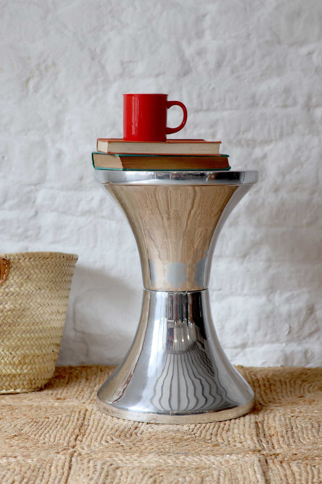 Small metallic side table with a red mug and books on a textured surface.
