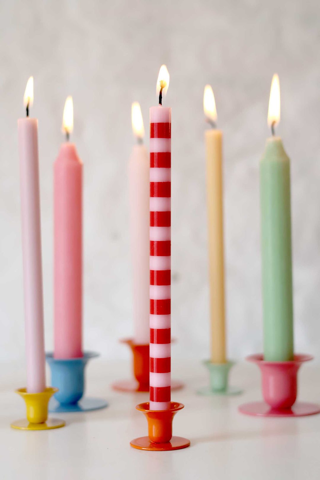 Colorful candles in various holders on a light background