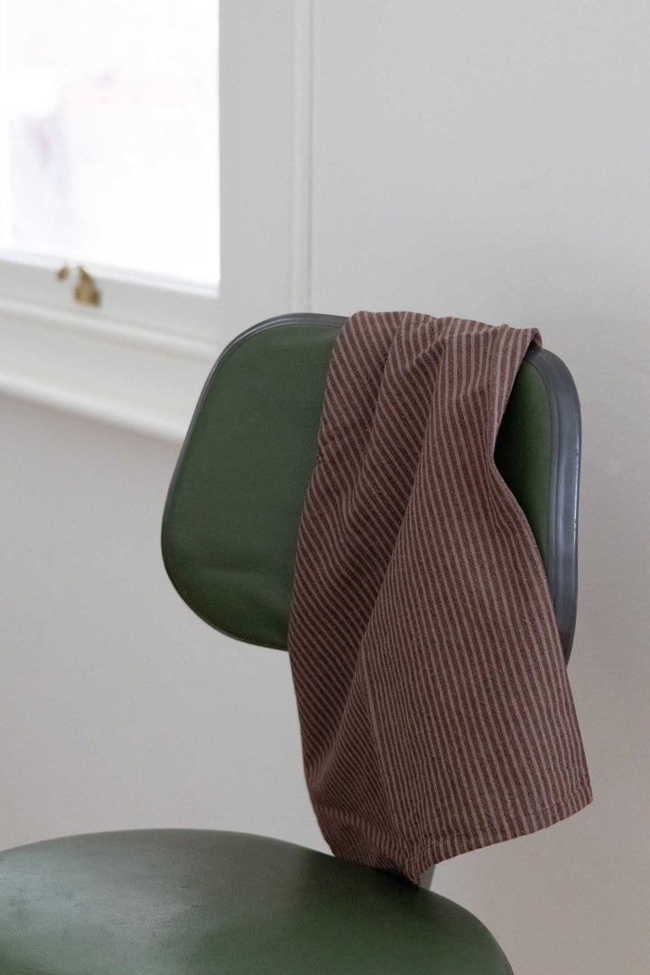 A brown corduroy throw blanket draped over the back of a dark green chair in a bright, minimalist room.