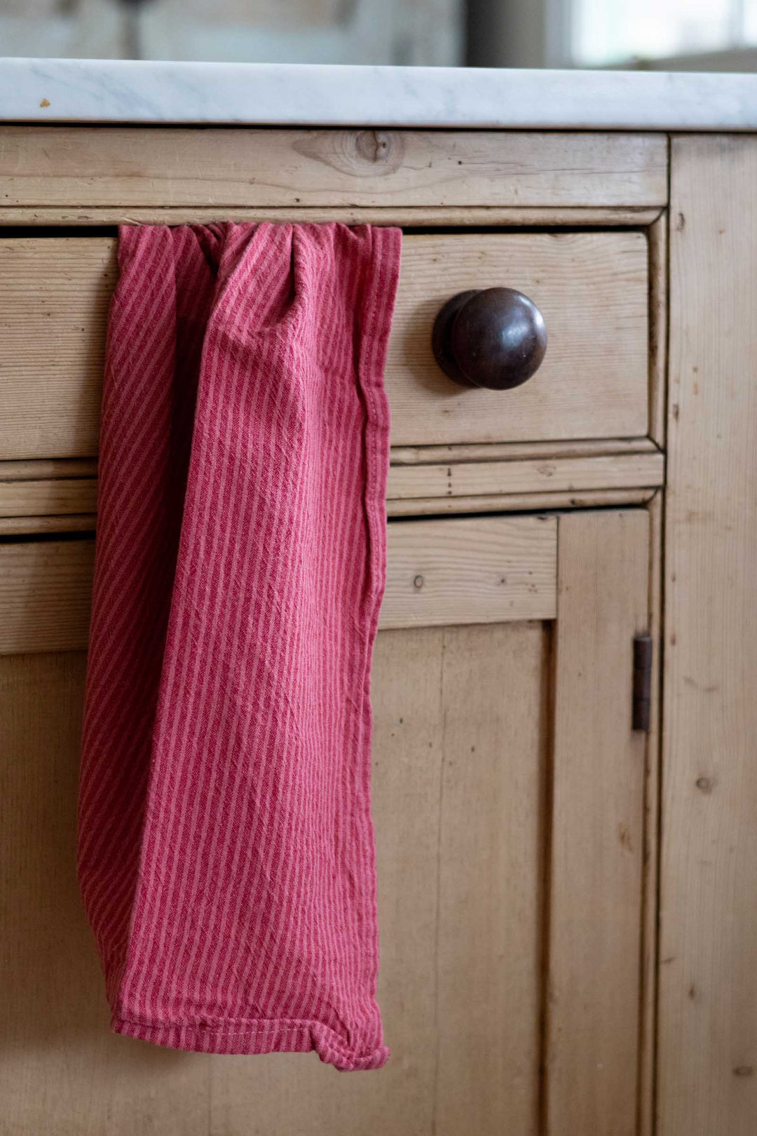 A pink ribbed cotton kitchen towel hanging from a drawer knob on a light wood cabinet.