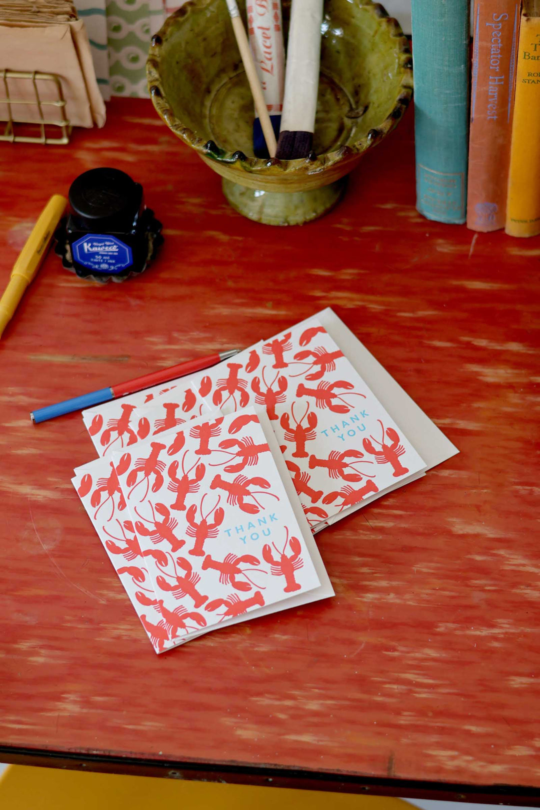 Two red lobster-patterned cards on a wooden surface with stationery items.