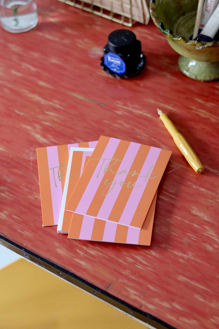 Stack of orange and pink striped cards on a red surface with inkwell and pen.