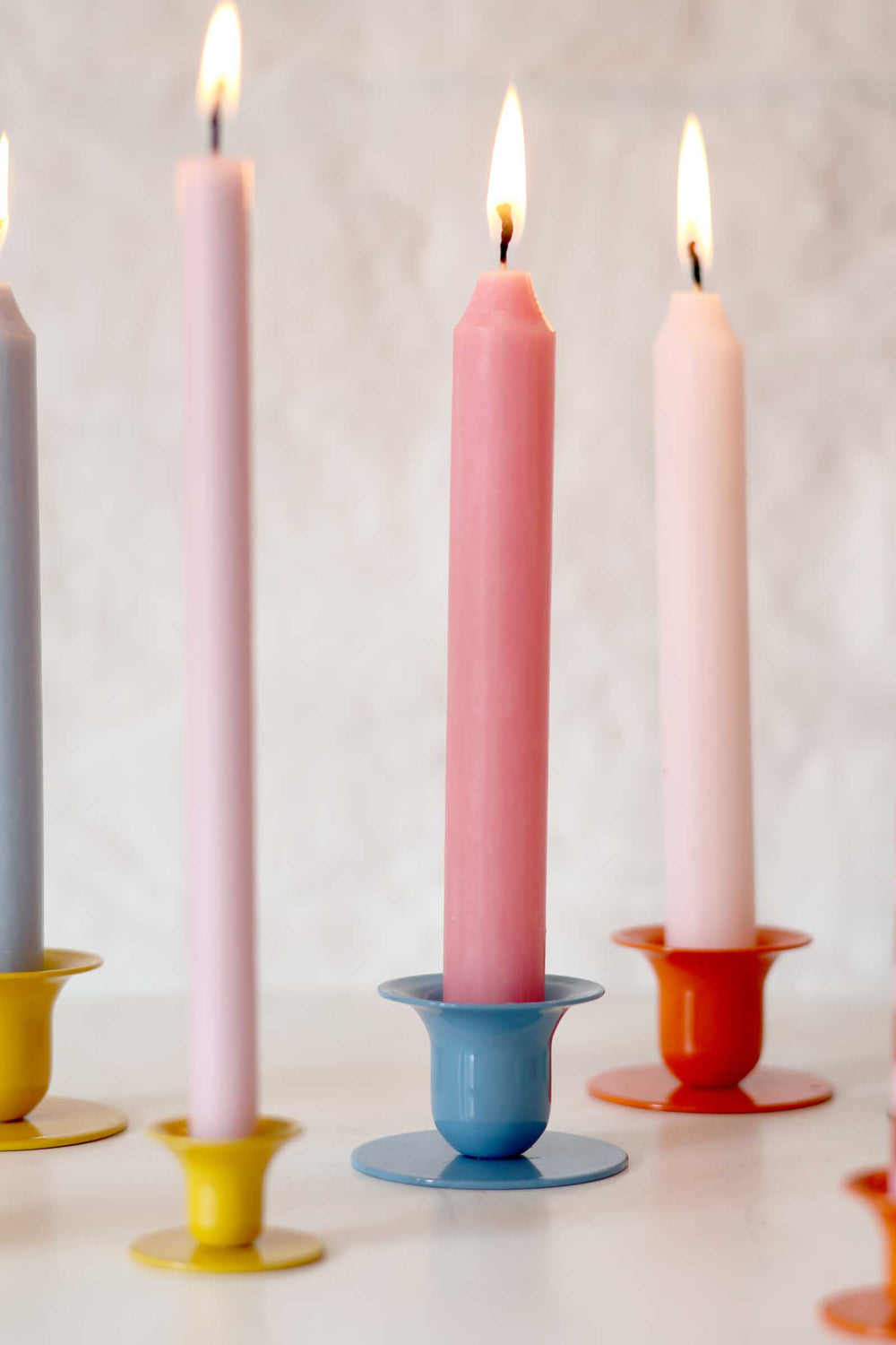 Three pink candles in colorful holders on a light background