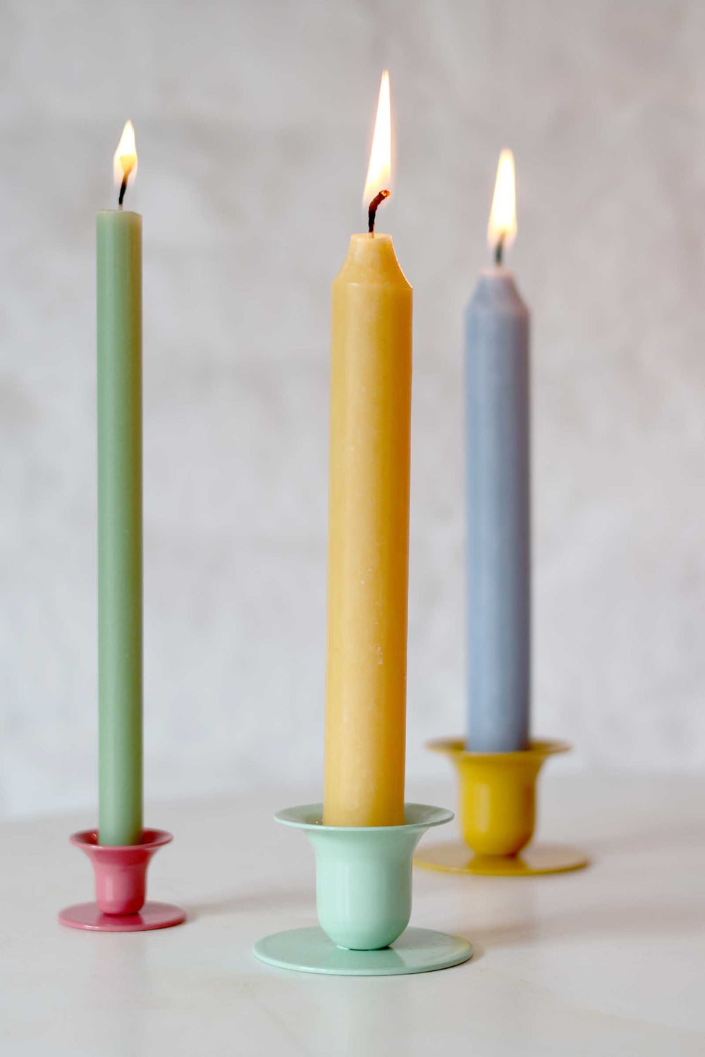 Three colorful candles in holders on a neutral background