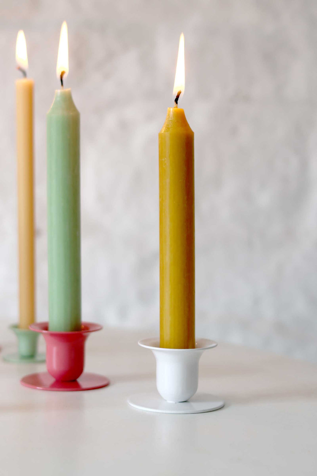 Three colorful candles in holders on a neutral background