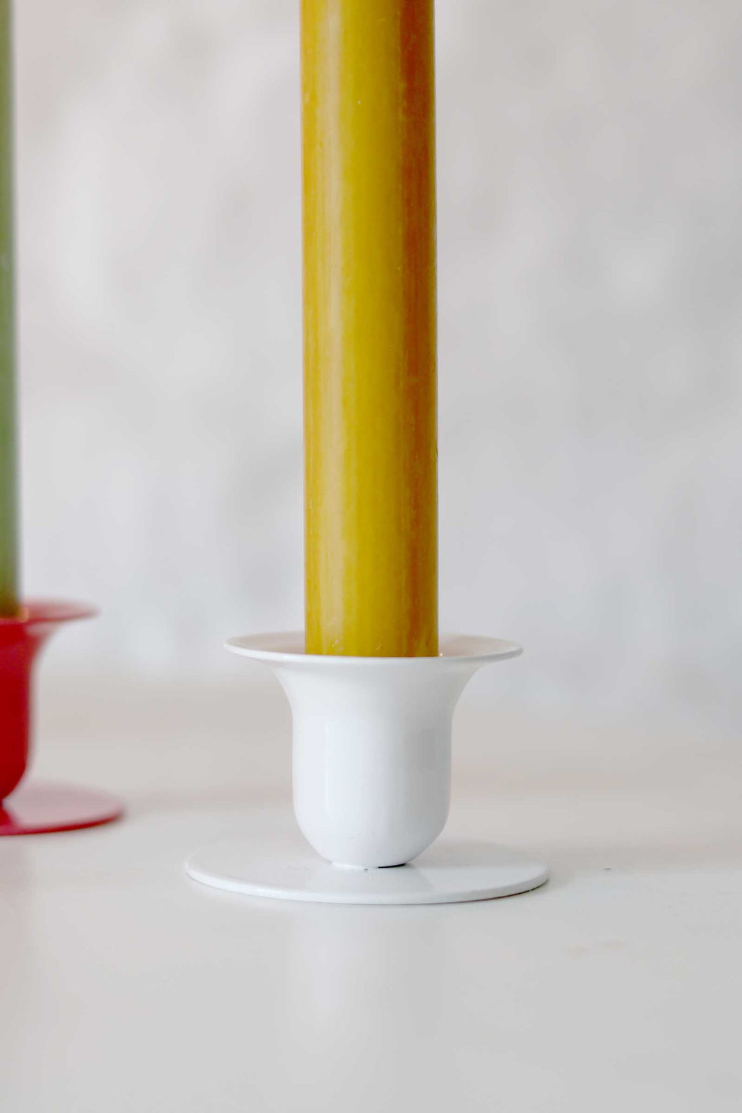Yellow candle in a white holder on a white surface with a light gray background