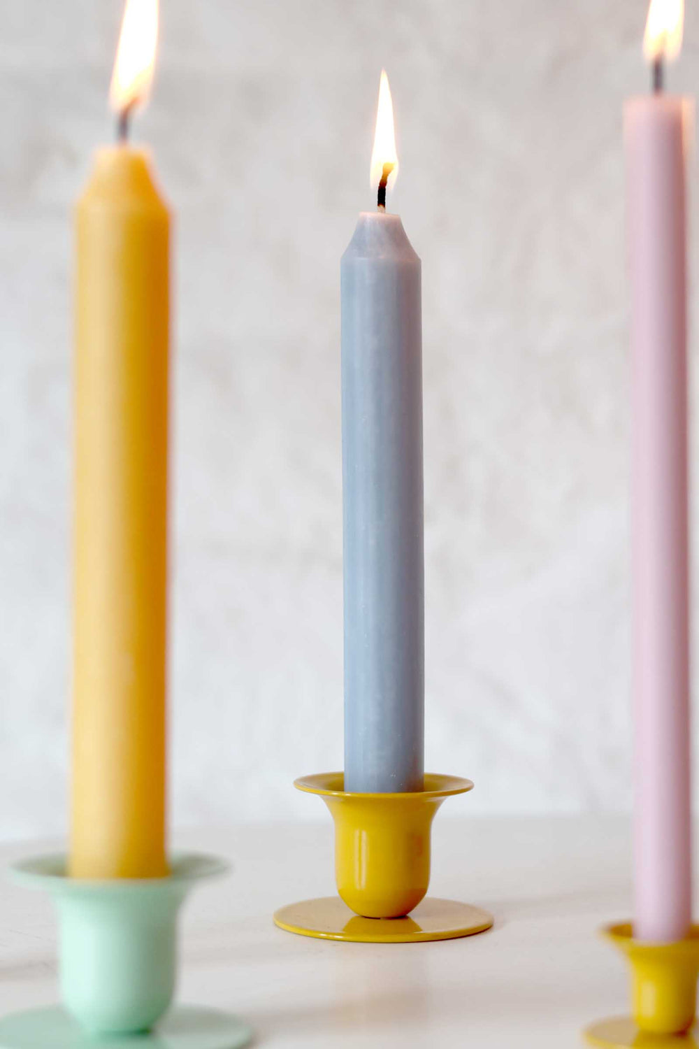 Three candles in different colors (yellow, gray, pink) on a white background