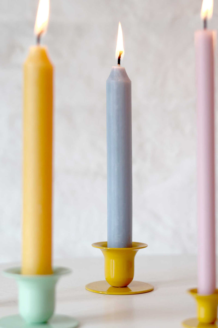 Three candles in different colors (yellow, gray, pink) on a white background
