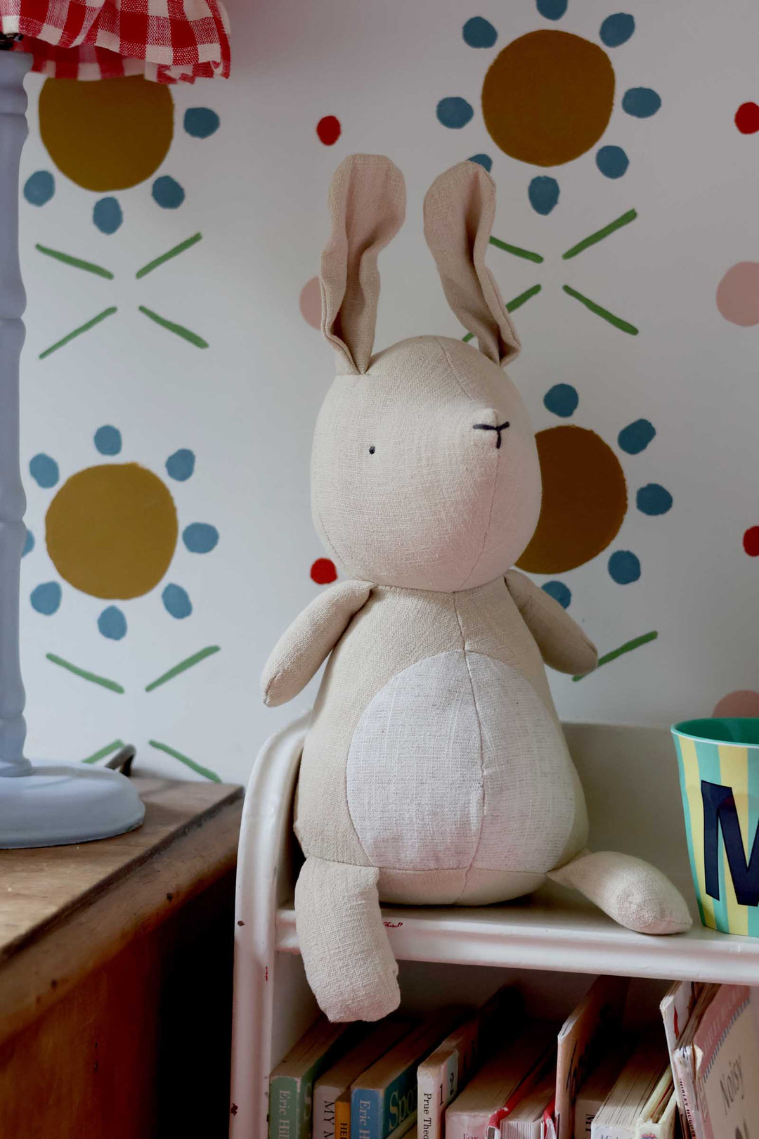 Stuffed rabbit toy on a shelf with a floral-patterned wall in the background