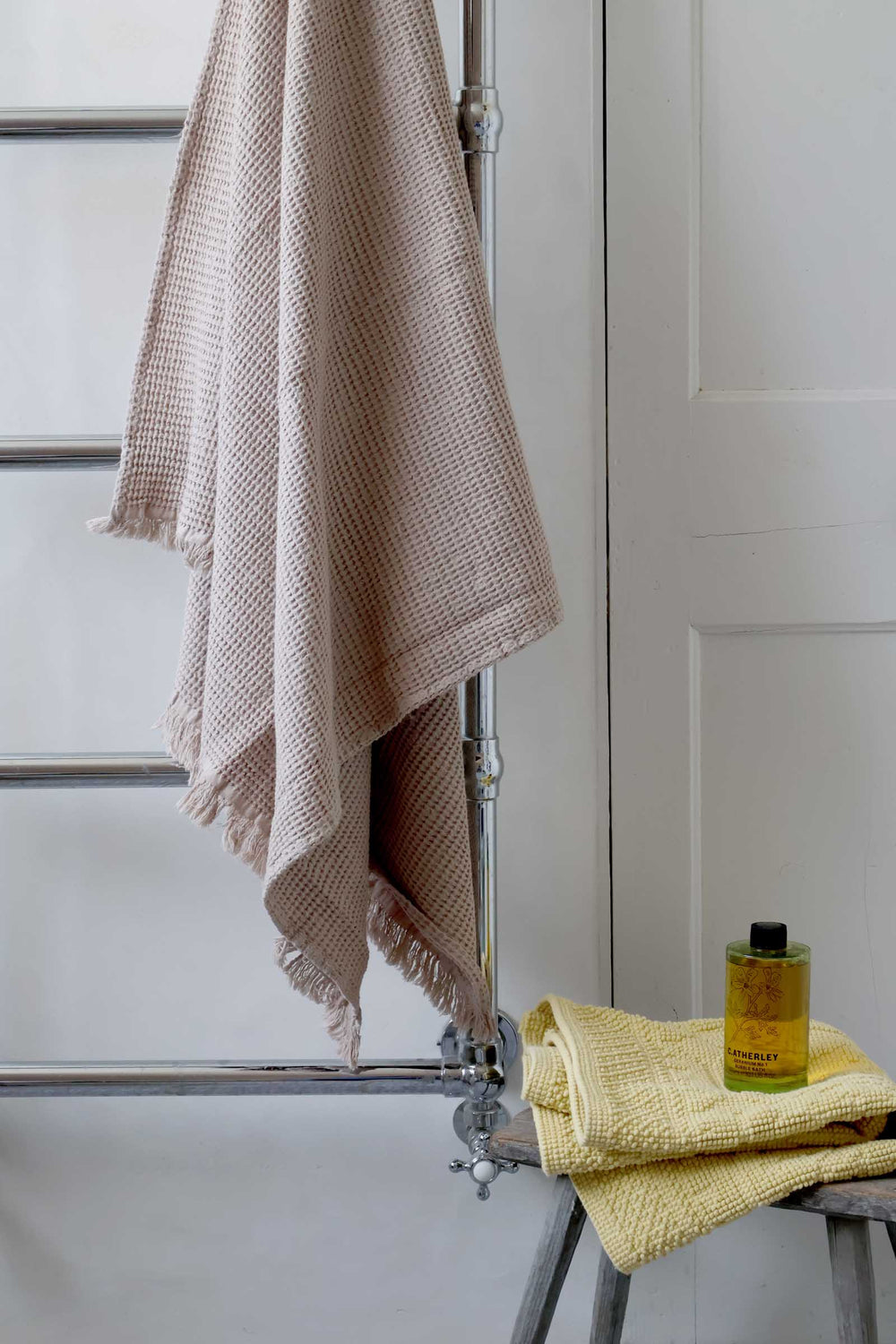 Towel hanging on a rack with a bottle of liquid soap on a stool in a bathroom setting.