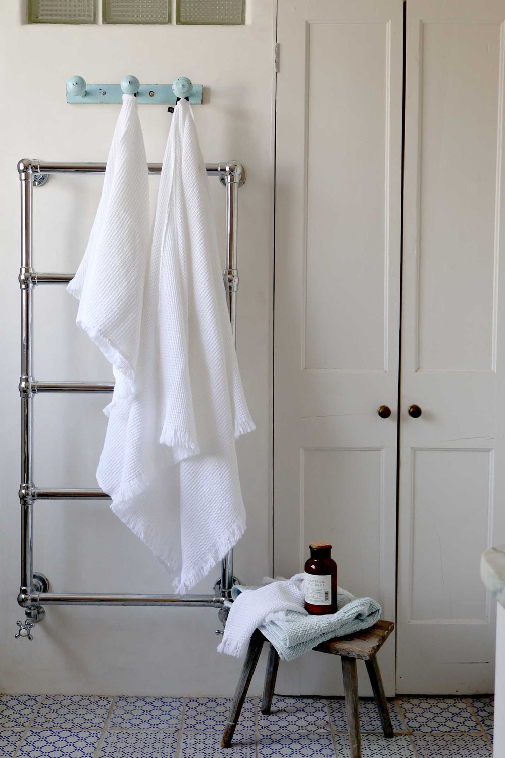 White towels hanging on a towel rack with a bottle and small stool in a bathroom setting.
