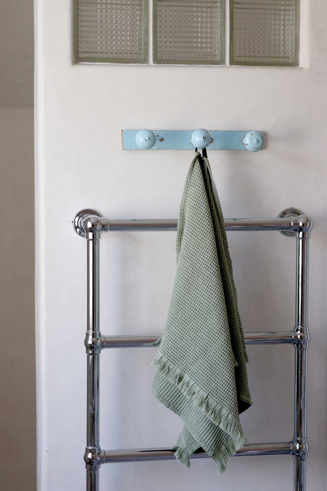 Towel rack with a green towel hanging on it against a white wall.