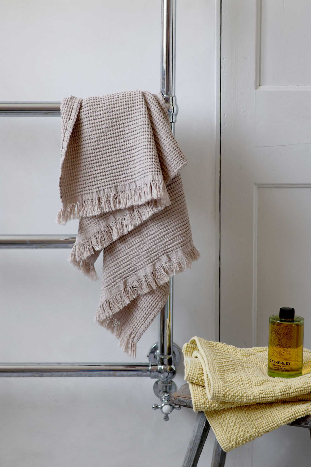 Towels hanging on a towel rack with a bottle of liquid soap in a bathroom setting.