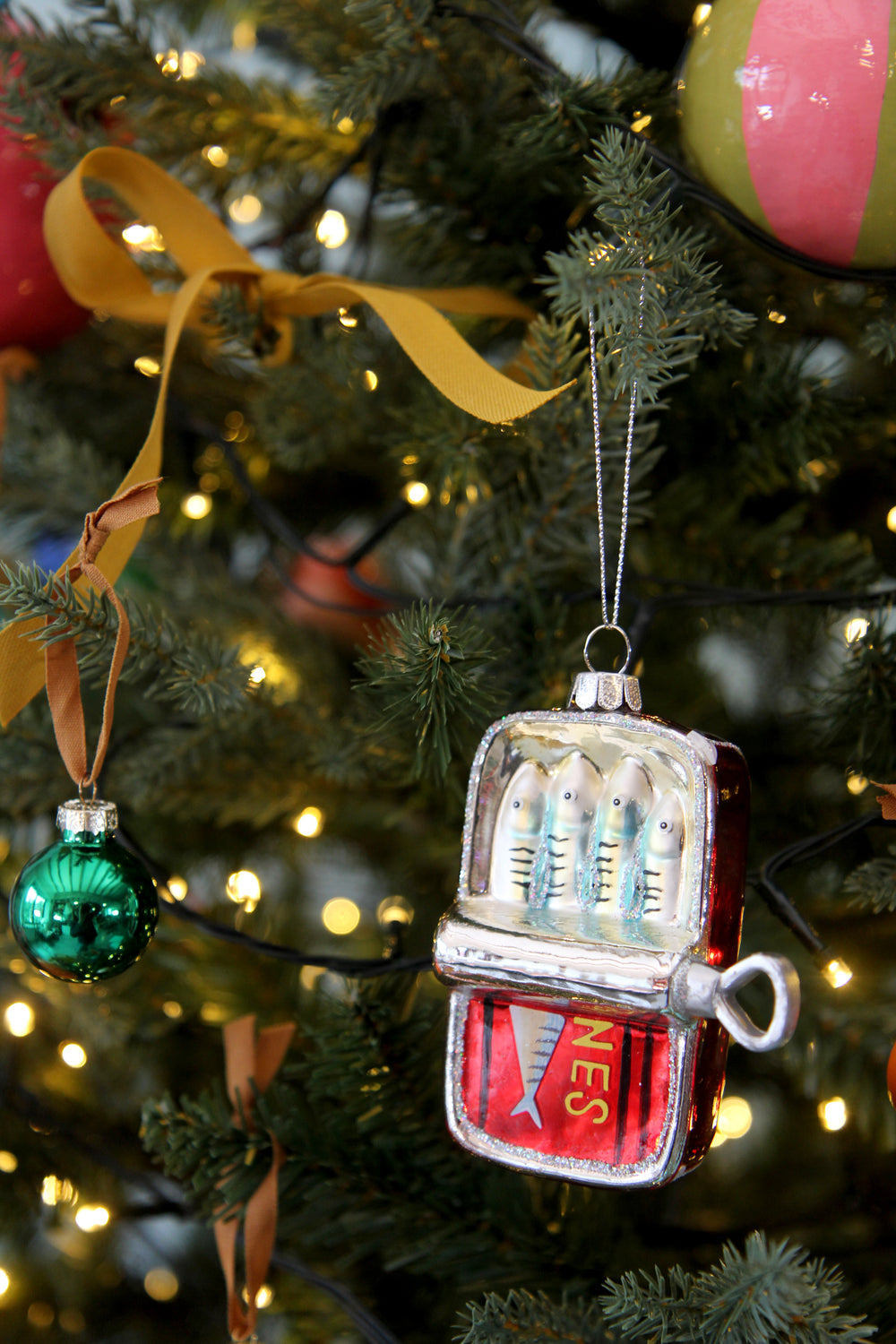 Decorative Christmas ornament shaped like a tin of sardines on a tree with lights in the background