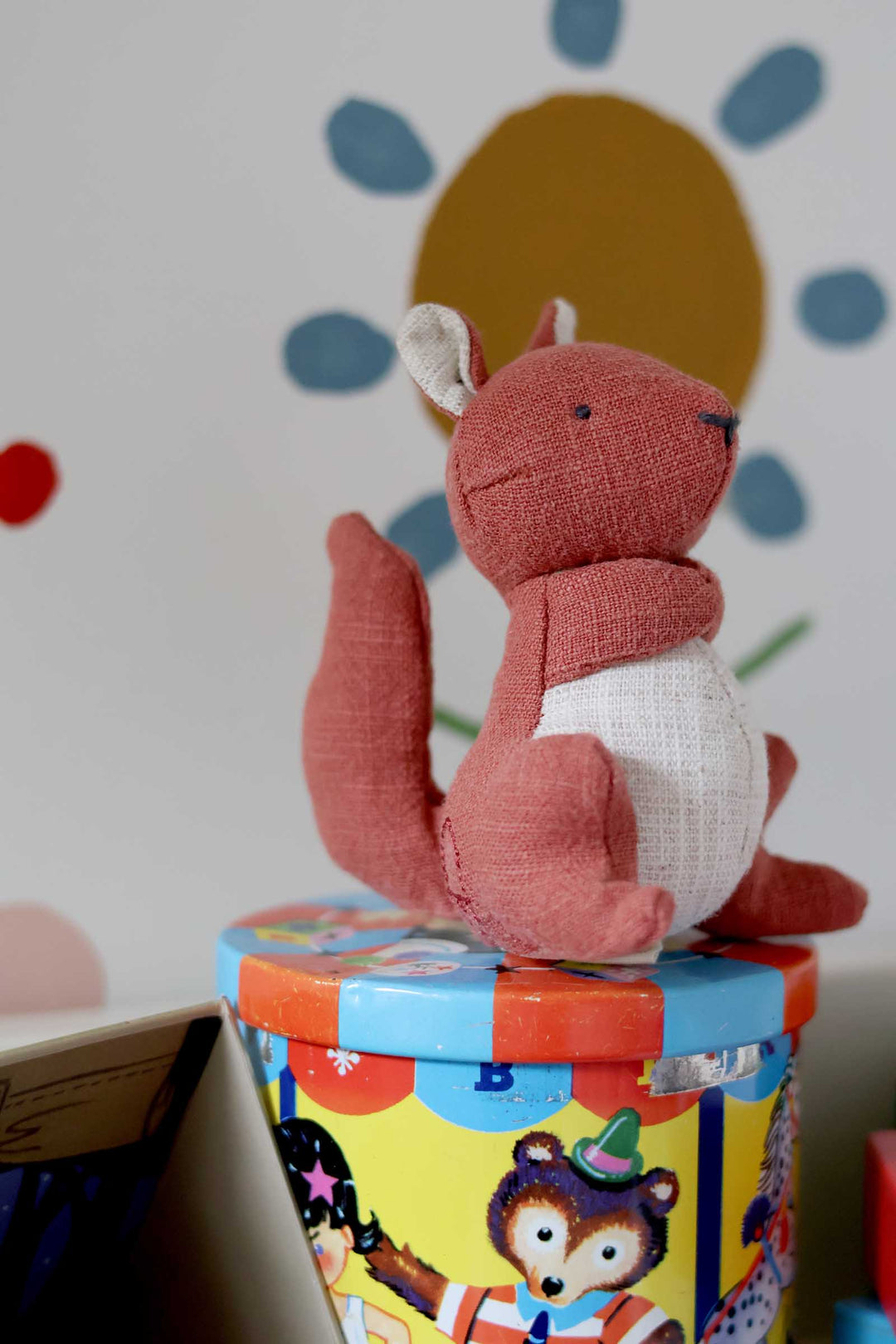 Red plush fox toy on a colorful box with a polka dot background