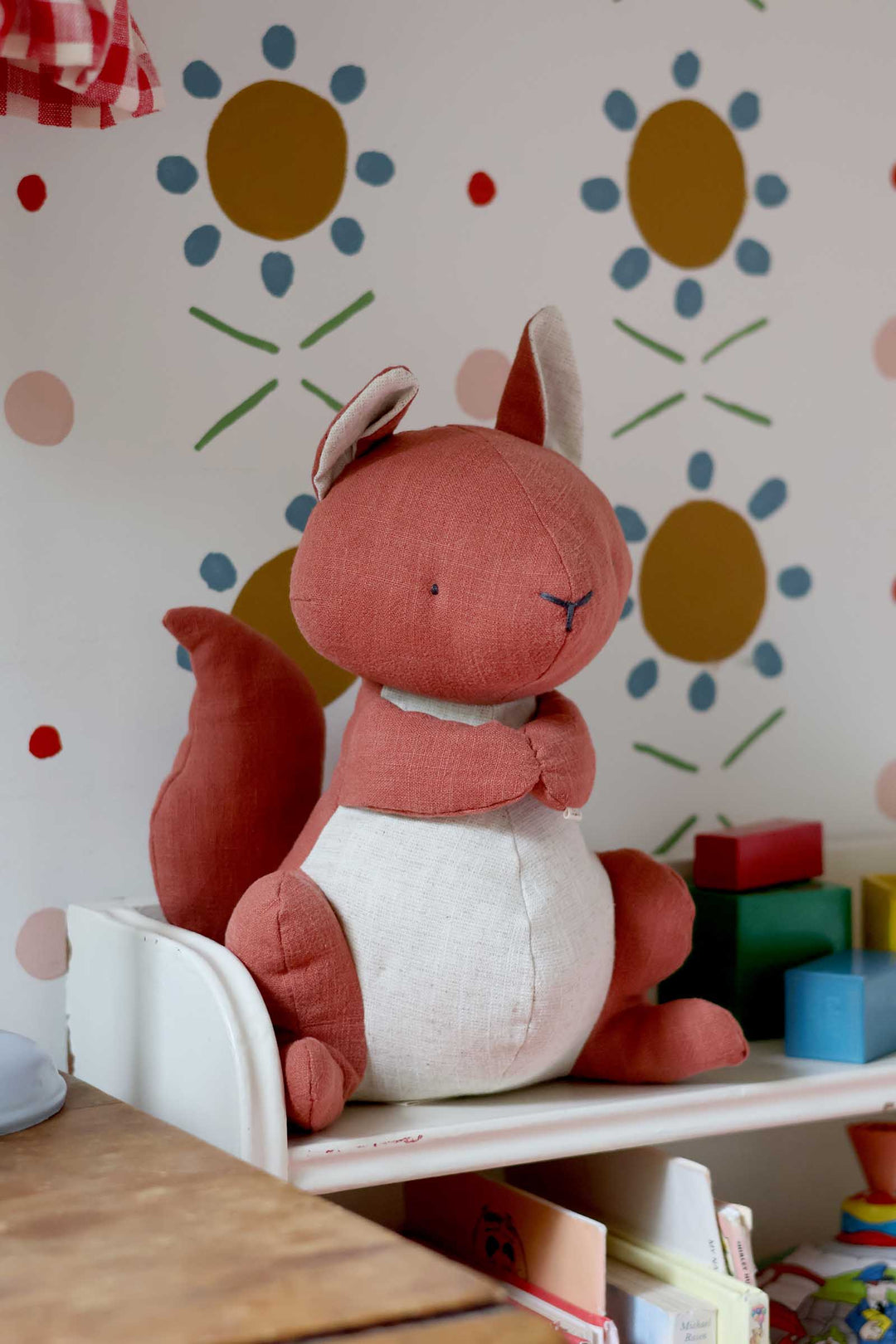 Plush squirrel toy on a shelf with colorful wall and toys in the background
